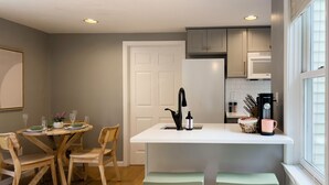 A modern kitchen with a central island, wooden chairs, a dining table, and a window with blinds. - Serenity Haven: A Modern Retreat (Monroe)