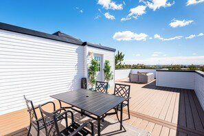 En tagterrasse med et bord og stole, plantekasser og udsigt til byens skyline.