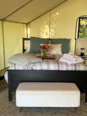 Ein Bett mit einer gestreiften Decke, Kissen, einer Vase mit Blumen und einem Nachttisch mit einer Lampe.