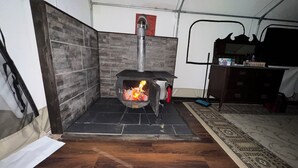 A room with a wood-burning stove, a tiled wall, a wooden floor, and a rug.