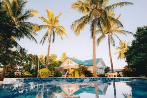 Une piscine entourée de palmiers et une maison avec un toit bleu.