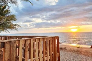 A wooden deck overlooking a beach with a sunset view.