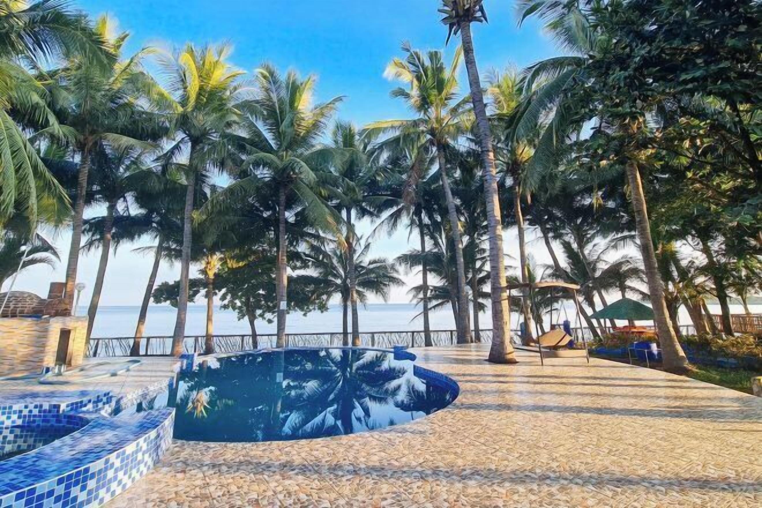 Zona de piscina con suelo de baldosas y palmeras.