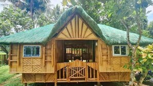 Une maison en bois avec un toit de chaume, entourée d’une végétation luxuriante.