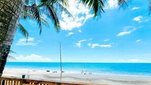 Une vue sur la plage, avec une clôture en bois, des palmiers et un ciel bleu dégagé.
