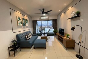 A modern living room with a sofa, ottoman, coffee table, TV, and a balcony with a city view. - Ipoh The Manhattan Suites Apartment by IWH (Ipoh)