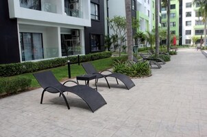 A paved walkway with outdoor seating and a building with balconies.