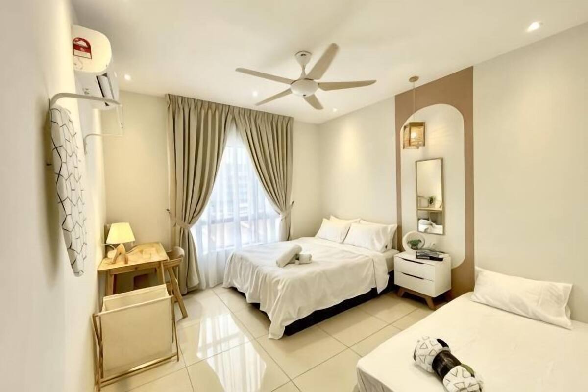 A hotel room with a bed, a desk, a chair, a ceiling fan, a window with curtains, and a mirror.