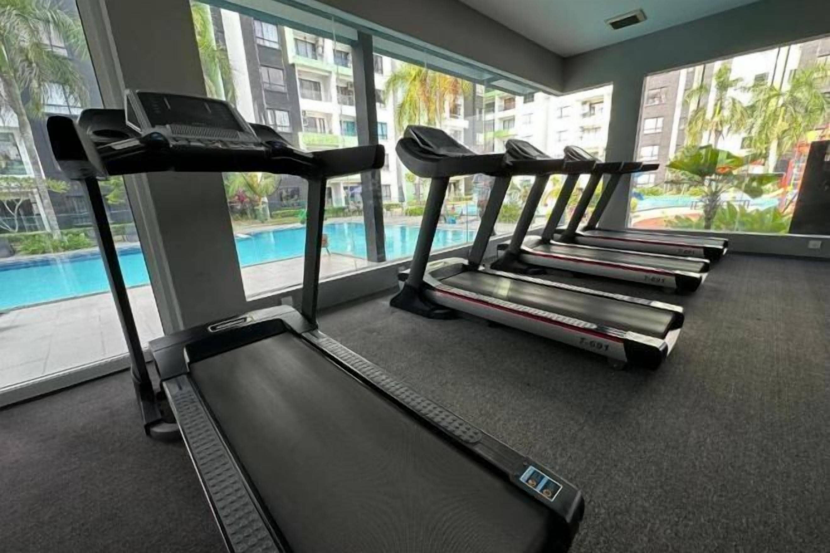 A gym with treadmills, a pool, and large windows with a view of palm trees.