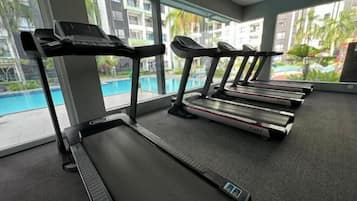 A gym with treadmills, a pool, and large windows with a view of palm trees.