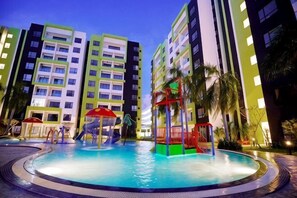 A swimming pool with a slide, surrounded by multi-story buildings with balconies. - Ipoh The Manhattan Suites Apartment by IWH (Ipoh)