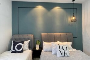 Une chambre à coucher avec deux lits, chacun doté d’une tête de lit et d’oreillers, une table de chevet avec une plante et un luminaire fixé au mur.