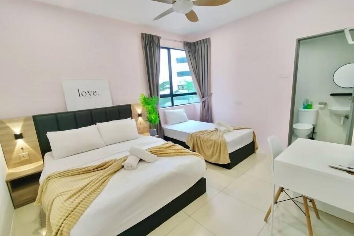 A hotel room with a bed, a desk, a chair, a ceiling fan, a window with curtains, and a sign that says 'love.'