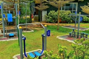 Ein Außenbereich zum Trainieren mit verschiedenen Fitnessgeräten, einem barrierefreien Weg und einem Gebäude im Hintergrund.