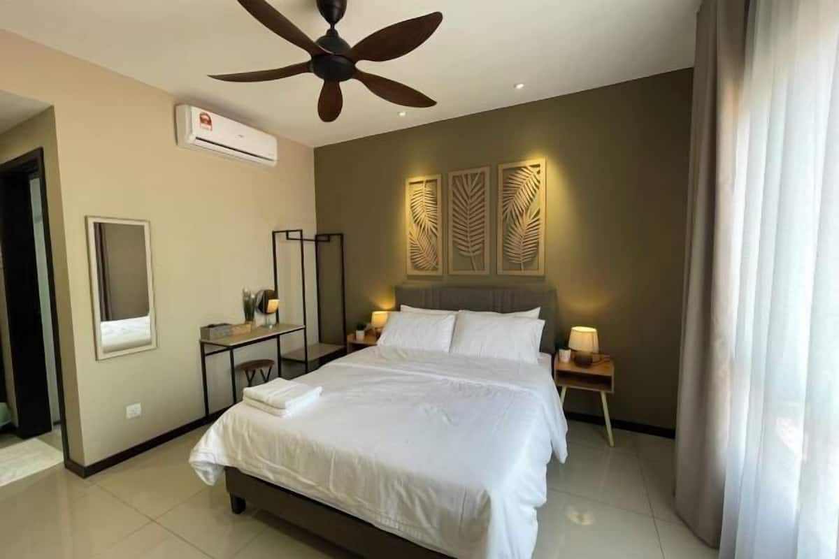 A hotel room with a bed, a ceiling fan, an air conditioning unit, a desk with a chair, and decorative wall panels.