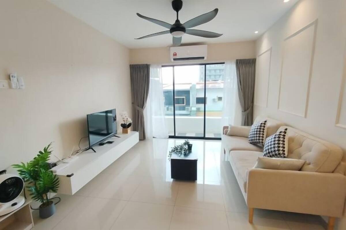 A modern living room with a flat-screen TV, a ceiling fan, a sofa, and a large window with curtains.