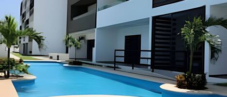 A modern building with a pool, surrounded by palm trees and a clear sky.