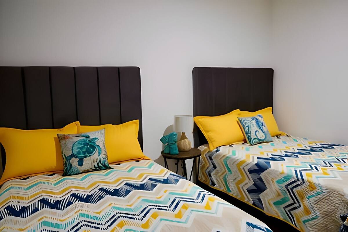Quarto de hotel com duas camas, cada uma com colcha estampada e almofadas amarelas.