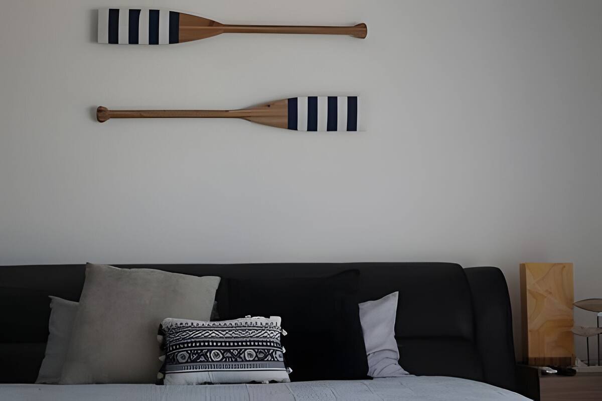 Quarto com sofá preto, duas paletas de madeira com listras pretas e brancas e almofada estampada.