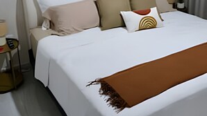 A neatly made bed with a white and brown bedspread, multiple pillows, and a decorative wall piece above it. - Marina cerritos Torre 1 (Mazatlán)