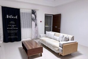 A modern living room with a white sofa, a wooden coffee table, and sheer curtains. - 1949 Dreamy Home (Panglao Municipality)