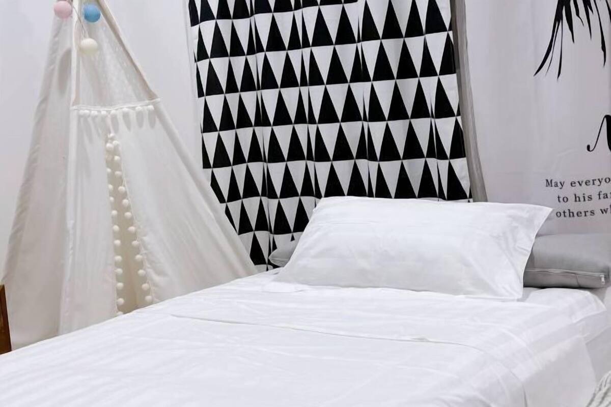A bed with white bedding, a black and white geometric curtain, and a white canopy with decorative elements.
