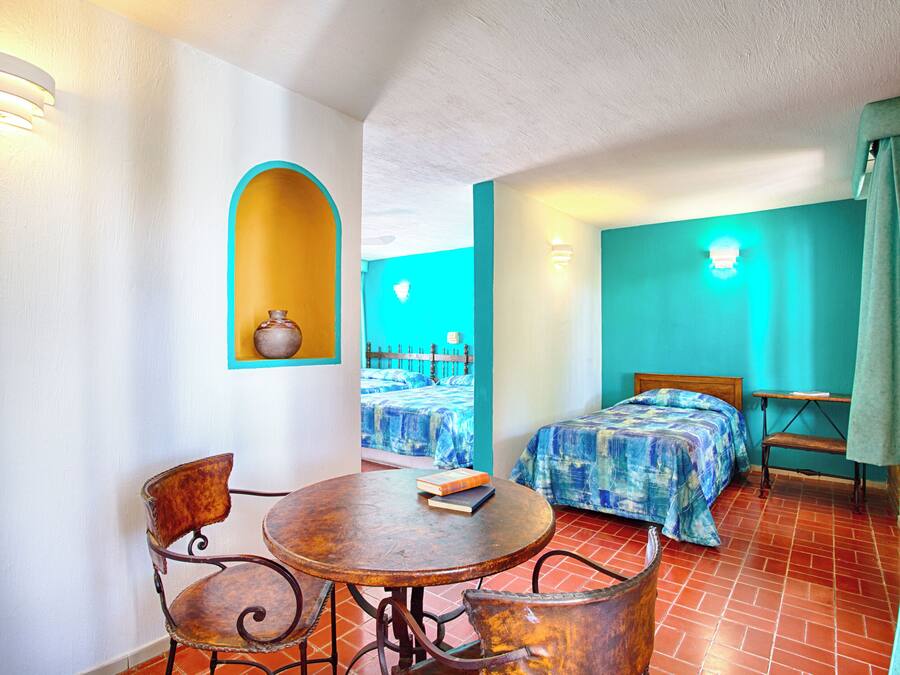 Una habitación con cama, una mesa con sillas y un pequeño rincón con un jarrón.