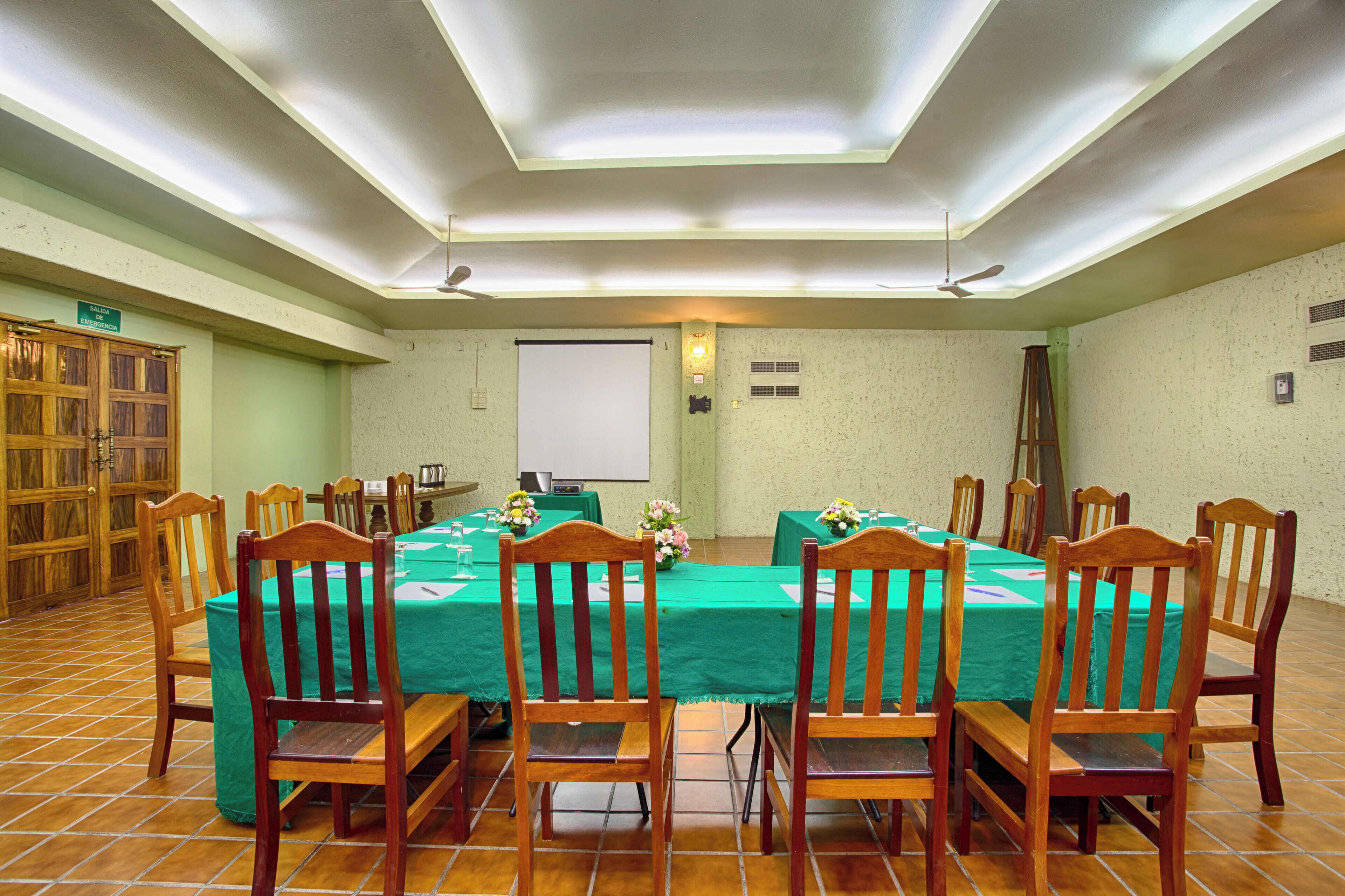 A conference room with a large table, chairs, a projector screen, and a speaker.