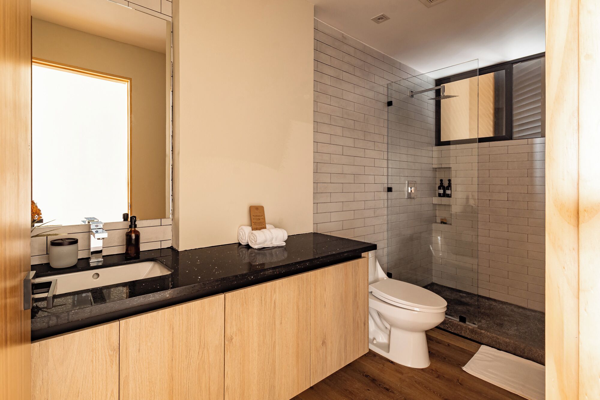 Une salle de bain moderne avec un plan de toilette noir, des meubles en bois, des toilettes blanches et une douche en verre.
