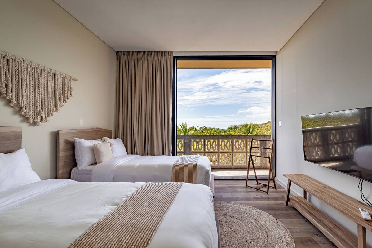 A hotel room with two beds, a large window with a view, a TV, and a balcony.