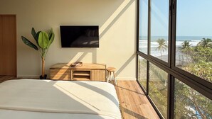 A bedroom with a large bed, a wooden nightstand, a television, and a view of the ocean. - Wave House (Chiltiupan)