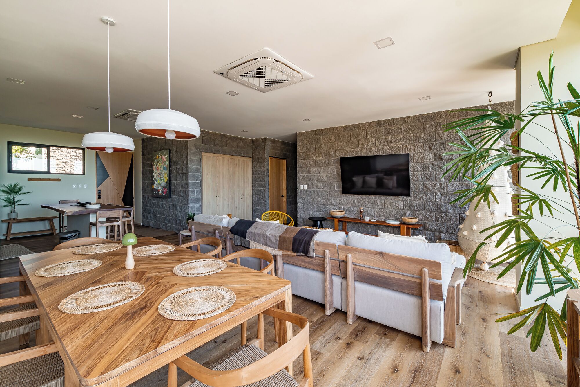 A modern living space with a dining area, sofa, and TV mounted on a stone wall.