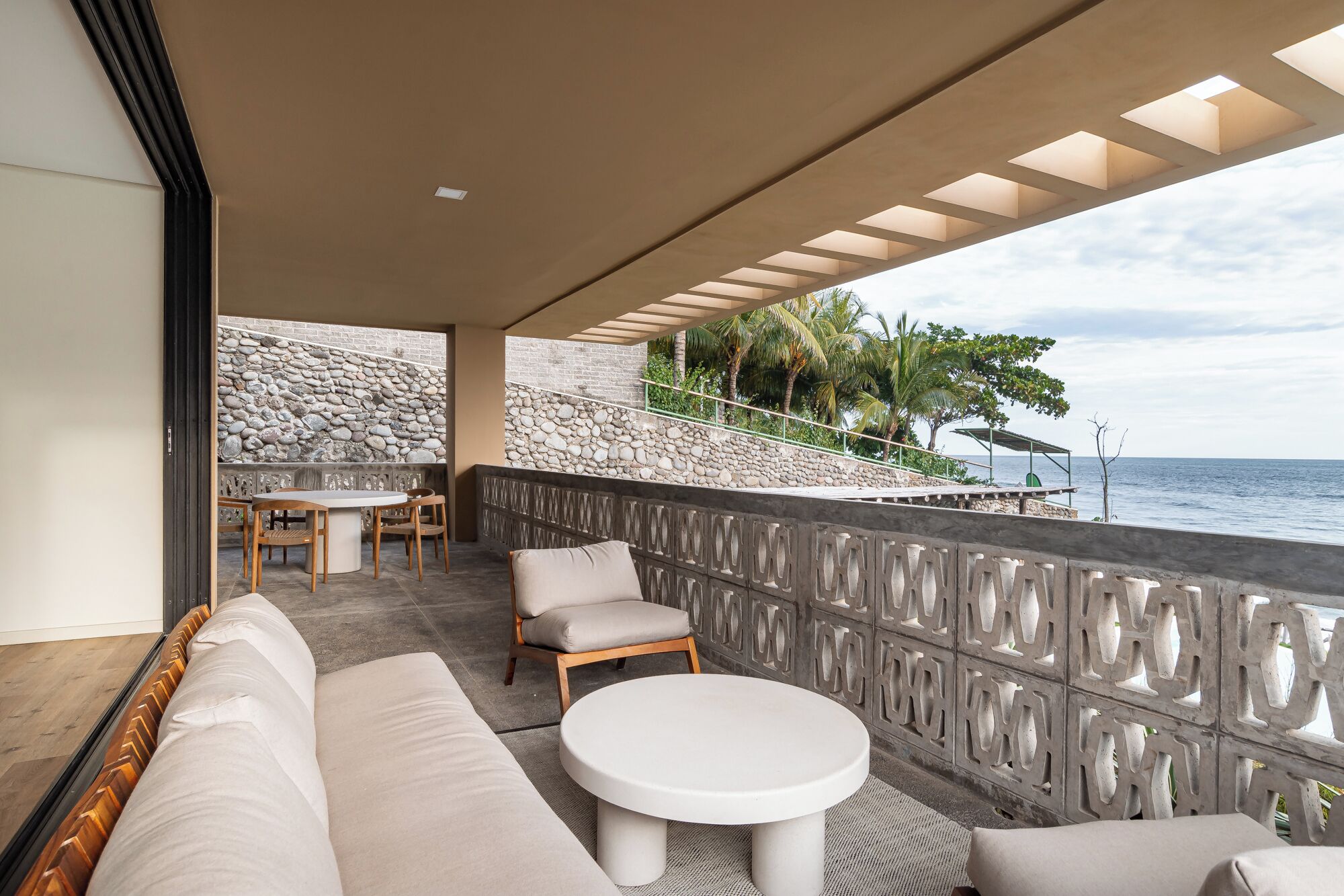 A balcony with a stone wall, a dining area, and a view of the ocean.