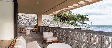 A balcony with a stone wall, a dining area, and a view of the ocean.