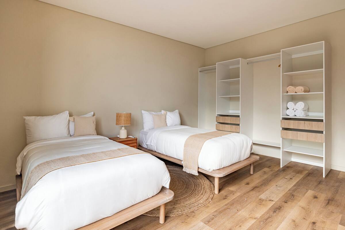 A bedroom with two beds, a bedside table with a lamp, and a wardrobe with shelves.