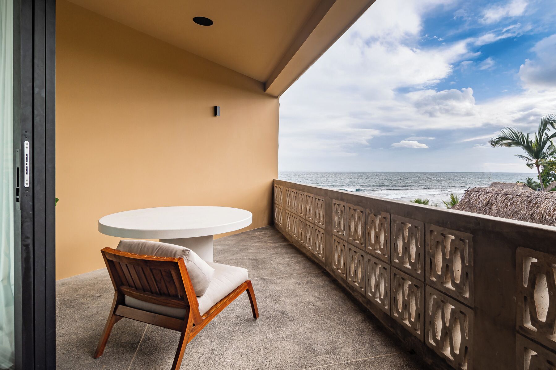 A balcony with a round table and a wooden chair, overlooking the ocean.