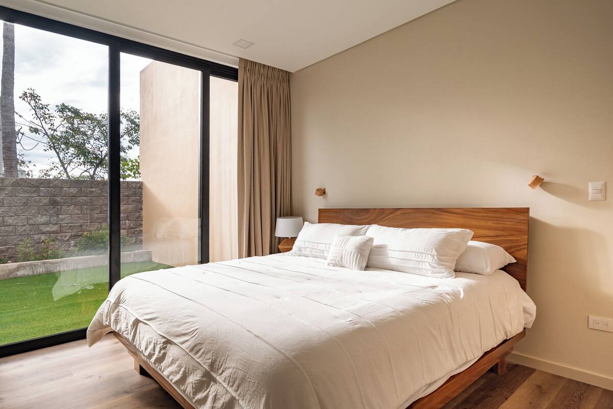 A bedroom with a large window, a wooden headboard, and a bed with white bedding.
