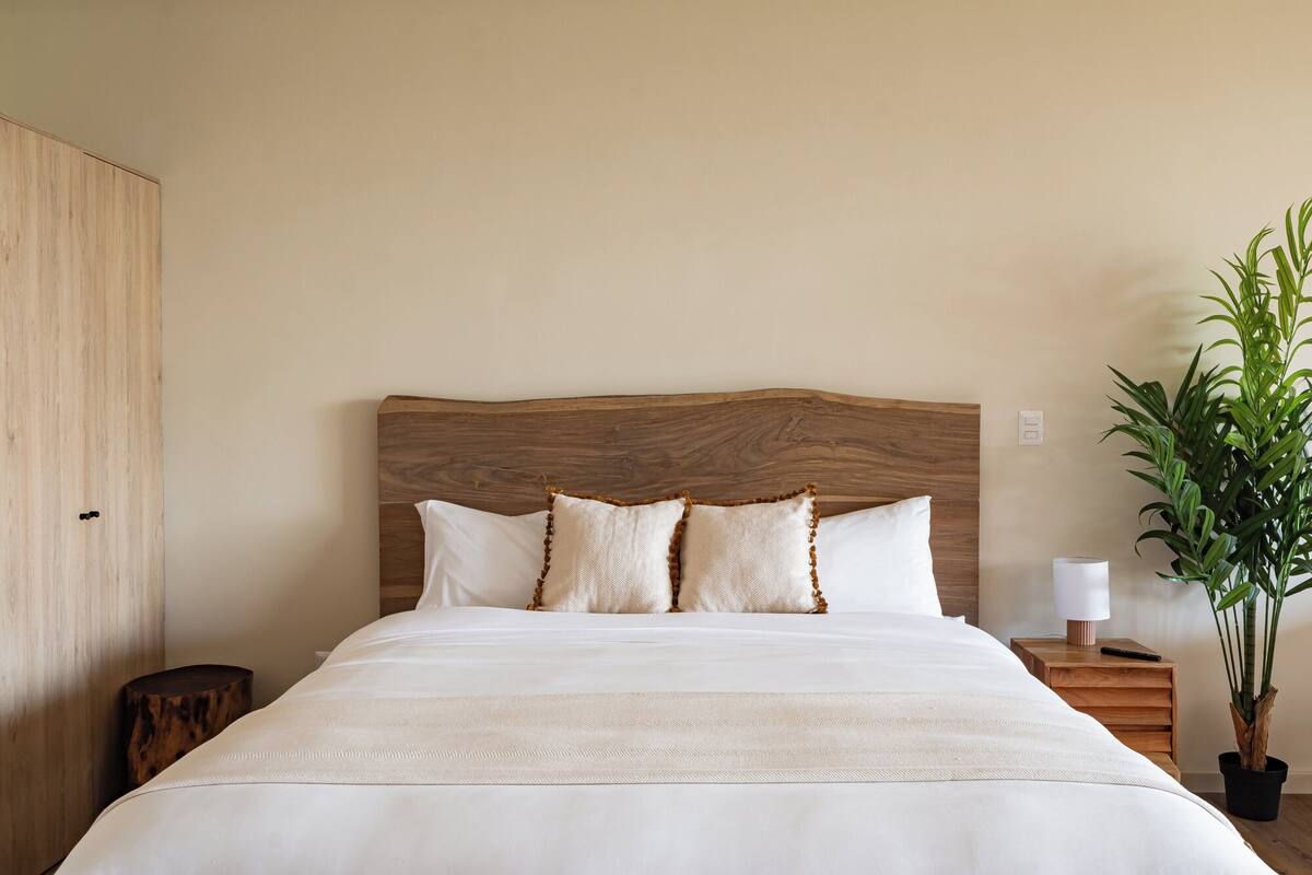 A neatly made bed with a wooden headboard, a bedside table with a lamp, and a potted plant.