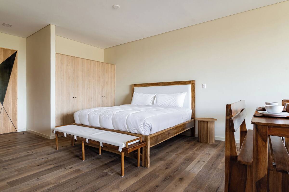 A bedroom with a wooden bed, a bench, a small round table, and a chair.