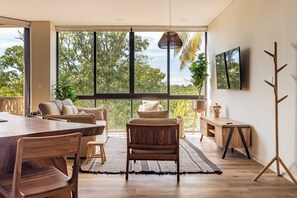 A spacious room with a large window, a dining area, and a seating area with a view of greenery.