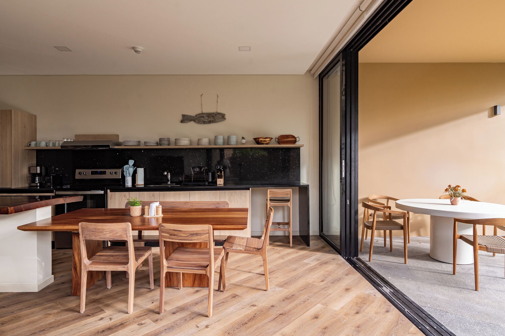 A modern kitchen with a black countertop, wooden chairs, and a dining table.