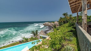 A beachfront property with a pool, thatched-roof structures, and lush greenery. - Wave House (Chiltiupan)