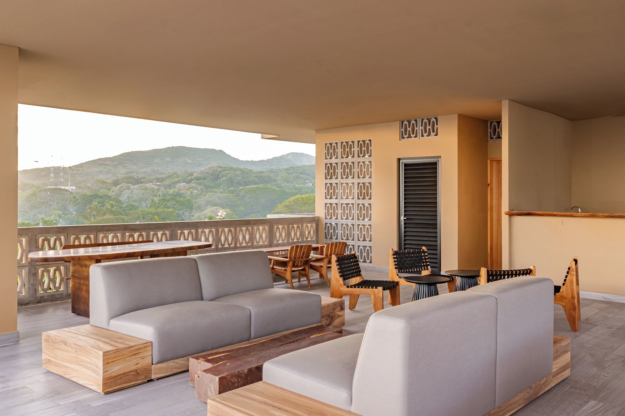 A balcony with a sofa, chairs, and a wooden coffee table. A patterned wall and a door are visible.