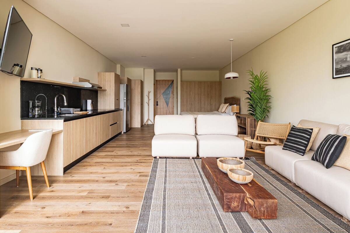 A modern living room with a sofa, a coffee table, and a dining area with a kitchen in the background.