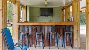 A rustic wooden bar area with a green wall, a flat-screen TV, and four metal bar stools. - Relax on the River - Waterfront Property (Maurepas)