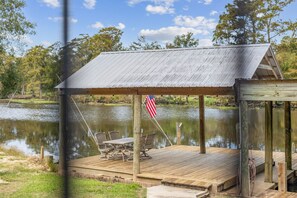 A wooden dock with a metal roof and a table with chairs, overlooking a calm body of water. - Relax on the River - Waterfront Property (Maurepas)
