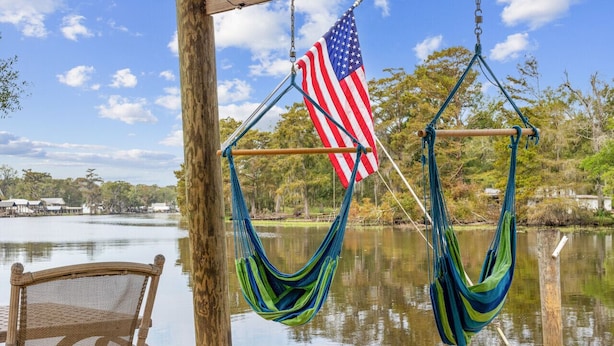 A hammock chair and hammock on a wooden deck by a lake with an American flag. - Relax on the River - Waterfront Property (Maurepas)