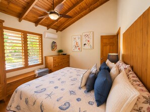 A bedroom with a wooden ceiling, a bed with a floral bedspread, a dresser, and a window with blinds.