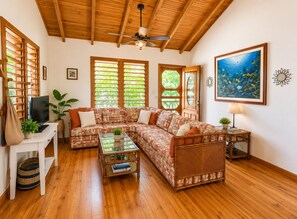 A living room with a sectional sofa, a television, a ceiling fan, and a painting of an underwater scene.