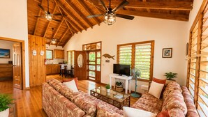 A spacious living area with a large sofa, a television, and a fan. - Calabash Reef House, 2 Bedrooms- Steps To The Ocean (Jose Santos Guardiola)